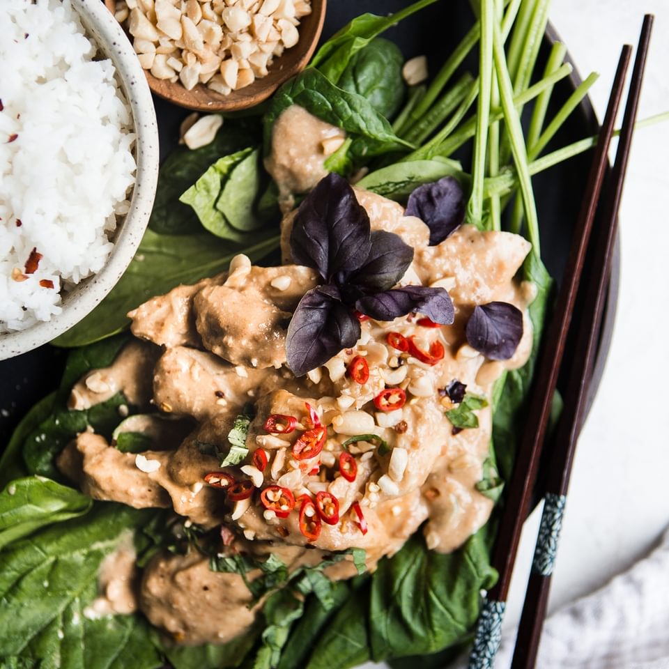 Slow Cooker Swimming Rama over spinach and peanuts on a plate with white rice and chop sticks