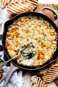 hot spinach artichoke dip in a cast iron pan with a spoon and grilled bread
