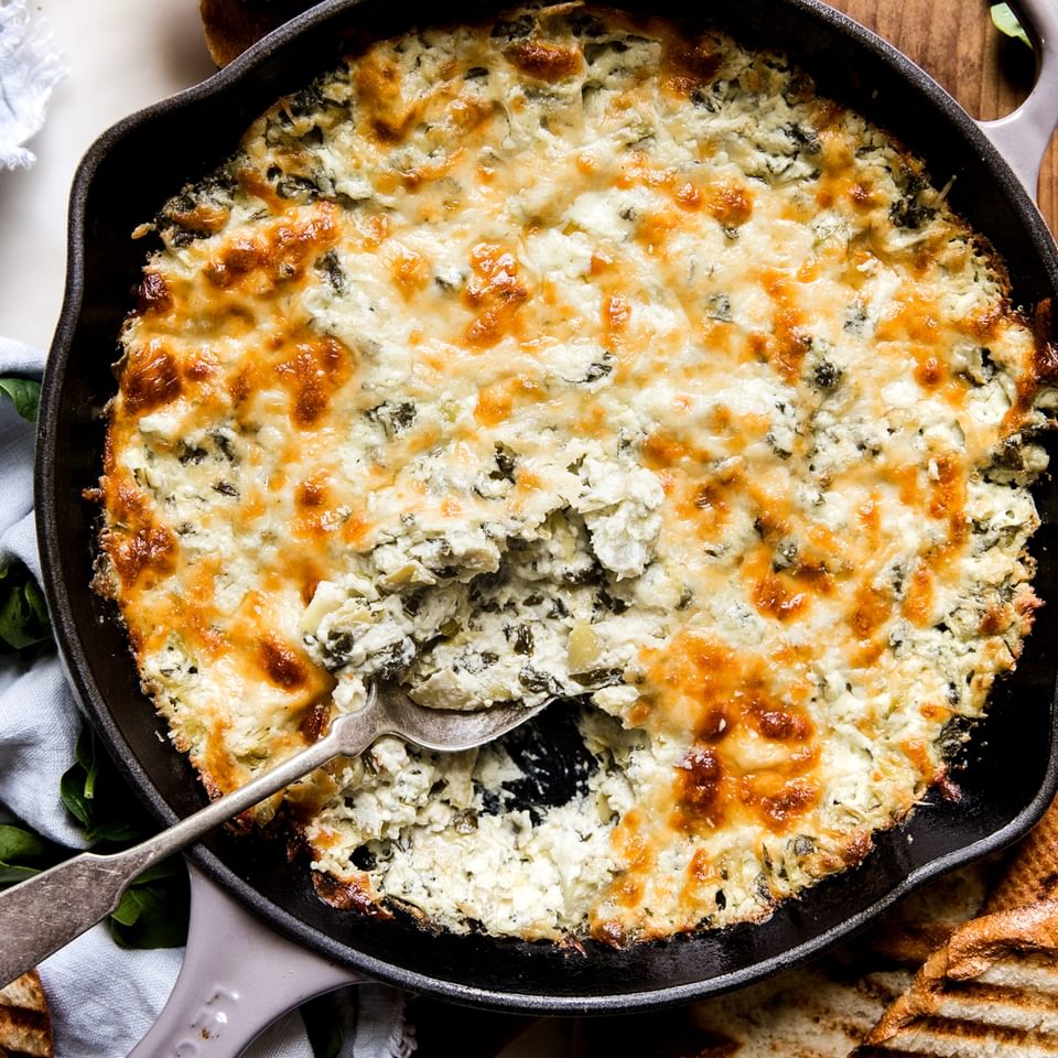 hot spinach artichoke dip in a cast iron pan with a spoon and grilled bread