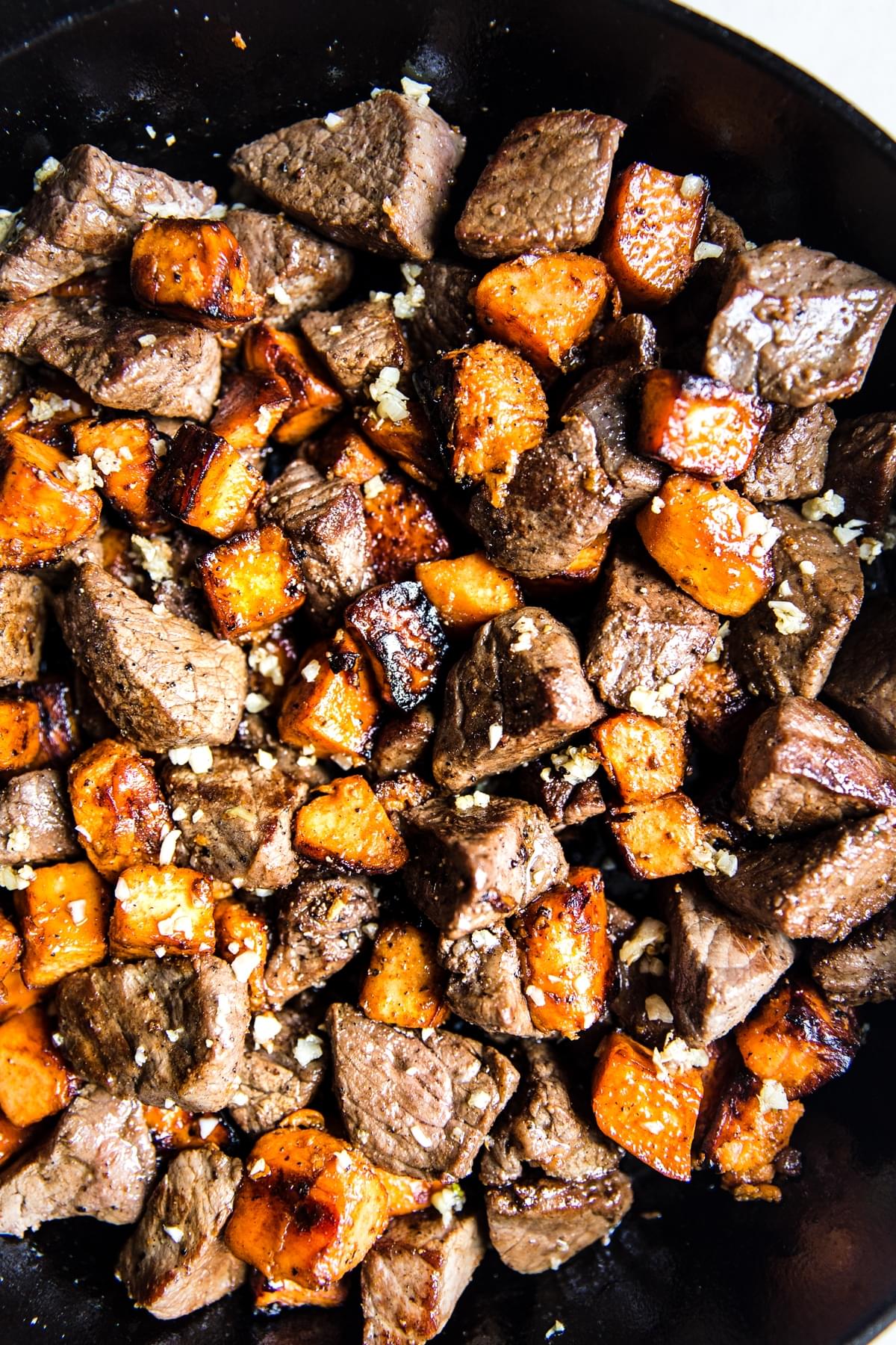 Garlic steak bites with sweet potatoes in a cast iron pan