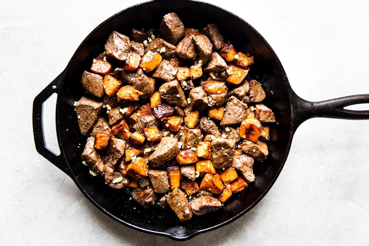 garlic steak and sweet potatoes cooked in a cast iron pan.