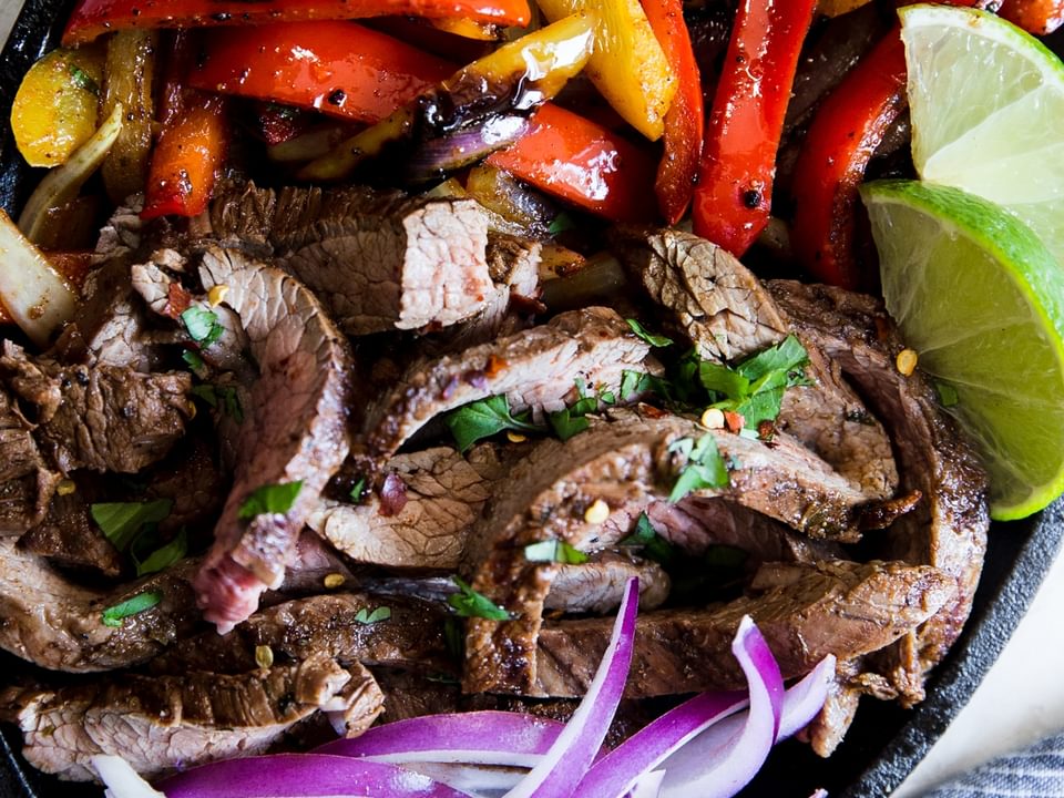 easy homemade steak fajitas in a skillet with onions, bell peppers and lime