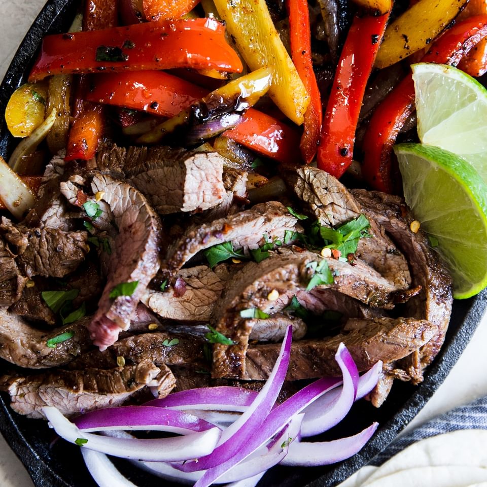 easy homemade steak fajitas in a skillet with onions, bell peppers and lime