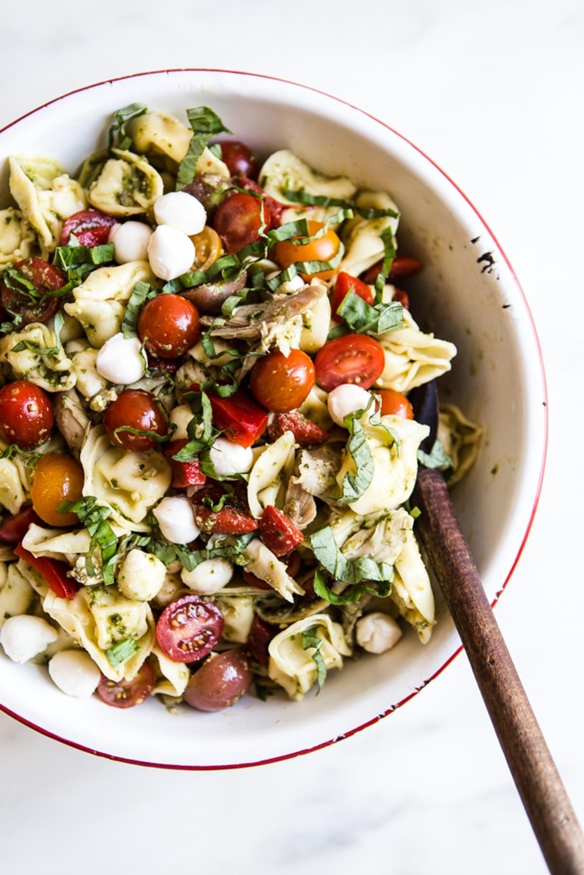 tortellini pasta salad in a bowl with pest, basil and tomatoes