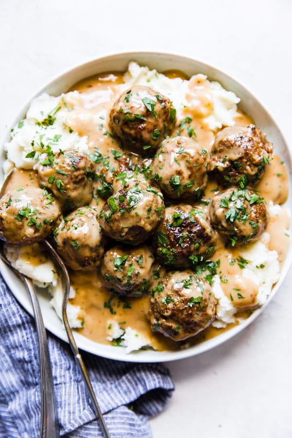 Easy swedish meatballs on a plate of mashed potatoes covered in creamy gravy and sprinkled with fresh parsley.