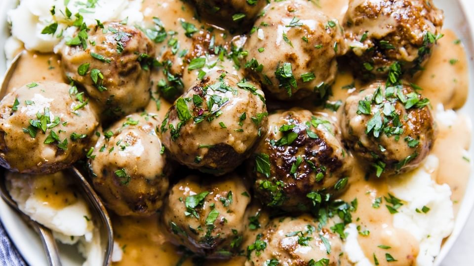 Easy swedish meatballs on a plate of mashed potatoes covered in creamy gravy and sprinkled with fresh parsley.