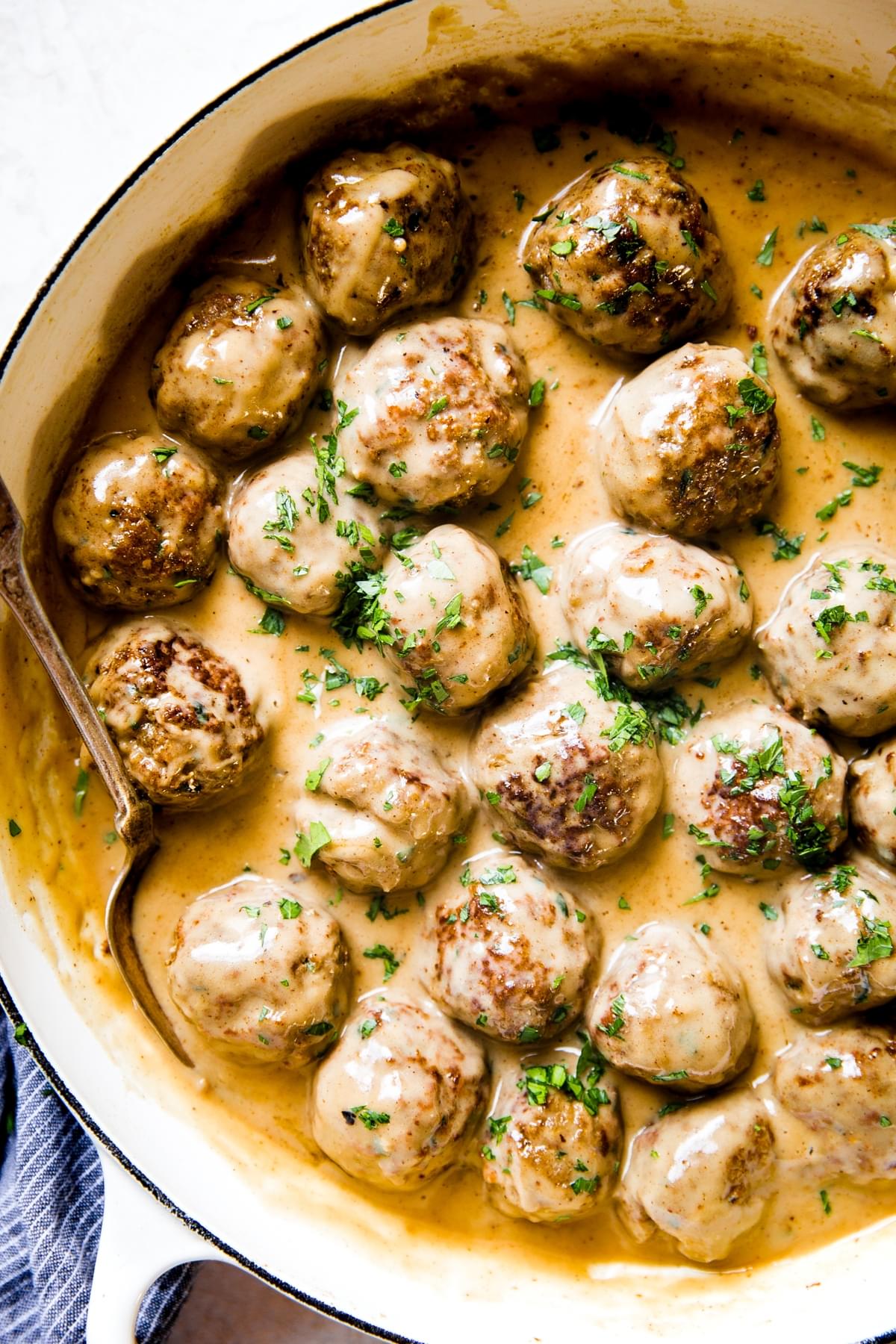 Swedish meatballs and creamy brown gravy in a pan with a serving spoon and linen.