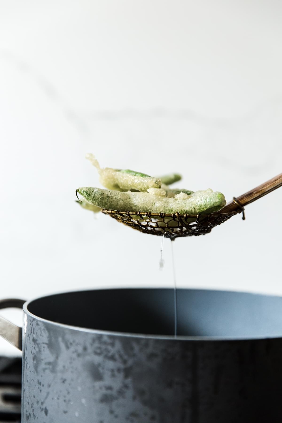 a slotted spoon filled with tempura green beans over a pot of oil in a pot