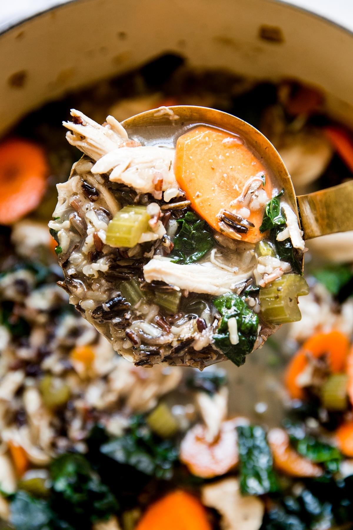 turkey and wild rice soup with carrots, celery, onion and kale in a ladle over a soup pot