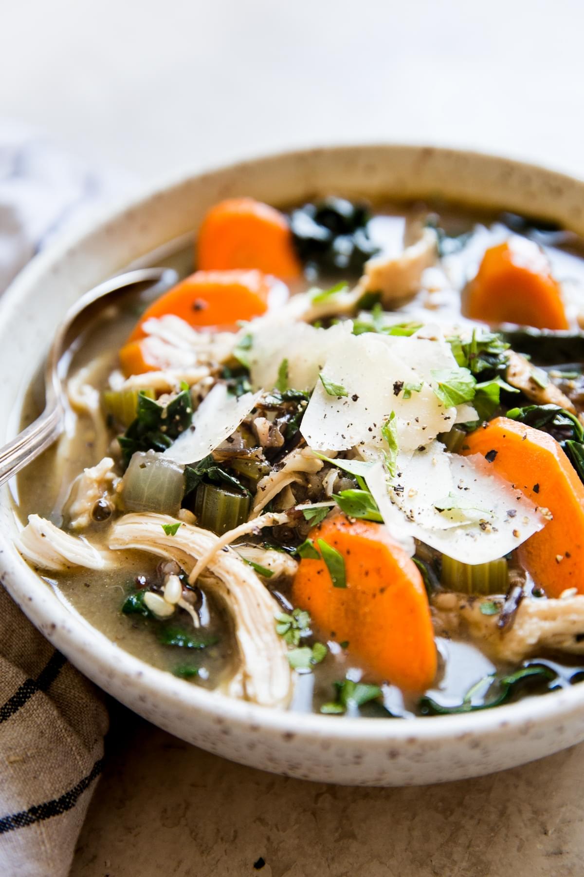 wild rice soup with turkey, carrots, celery and onions in a bowl with a spoon