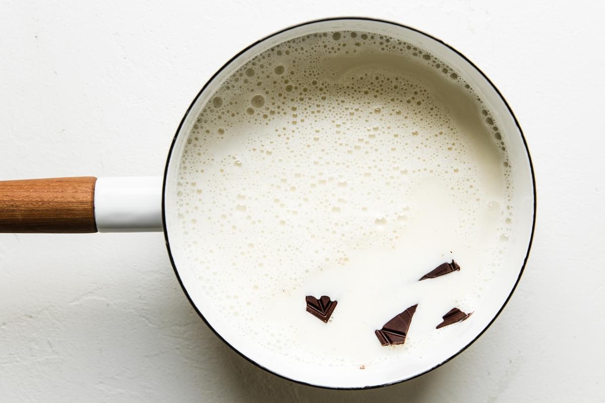 hot milk with chunks of dark chocolate in a white saucepan