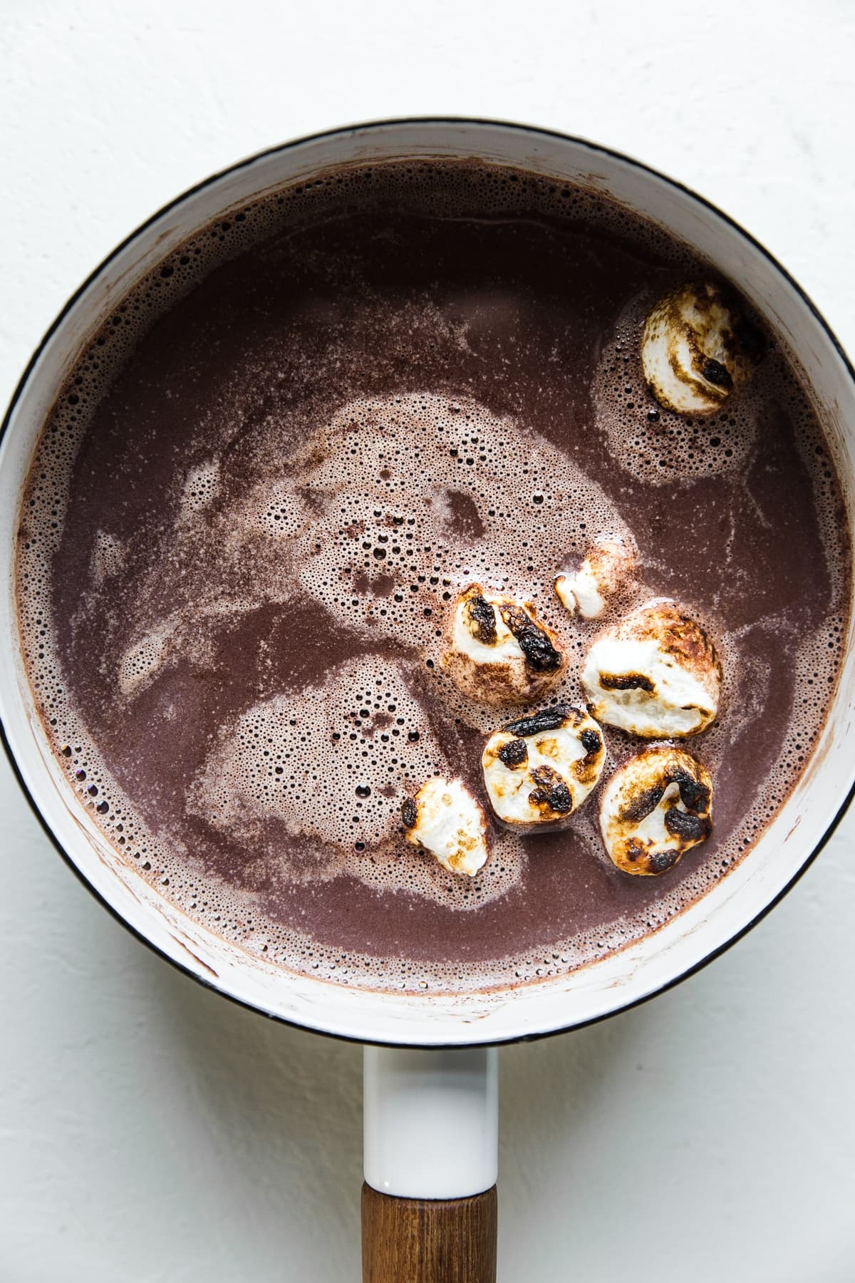 white enamel pot of hot chocolate topped with toasted marshmallows
