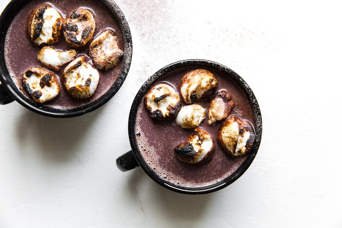 two black mugs of alcoholic hot chocolate top with toasted marshmallows