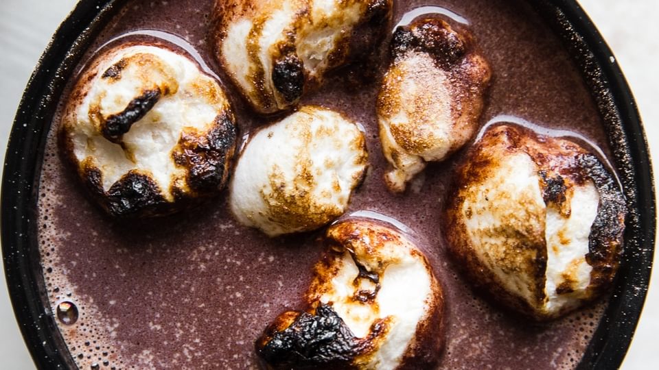 black mug of adult hot chocolate topped with toasted marshmallows