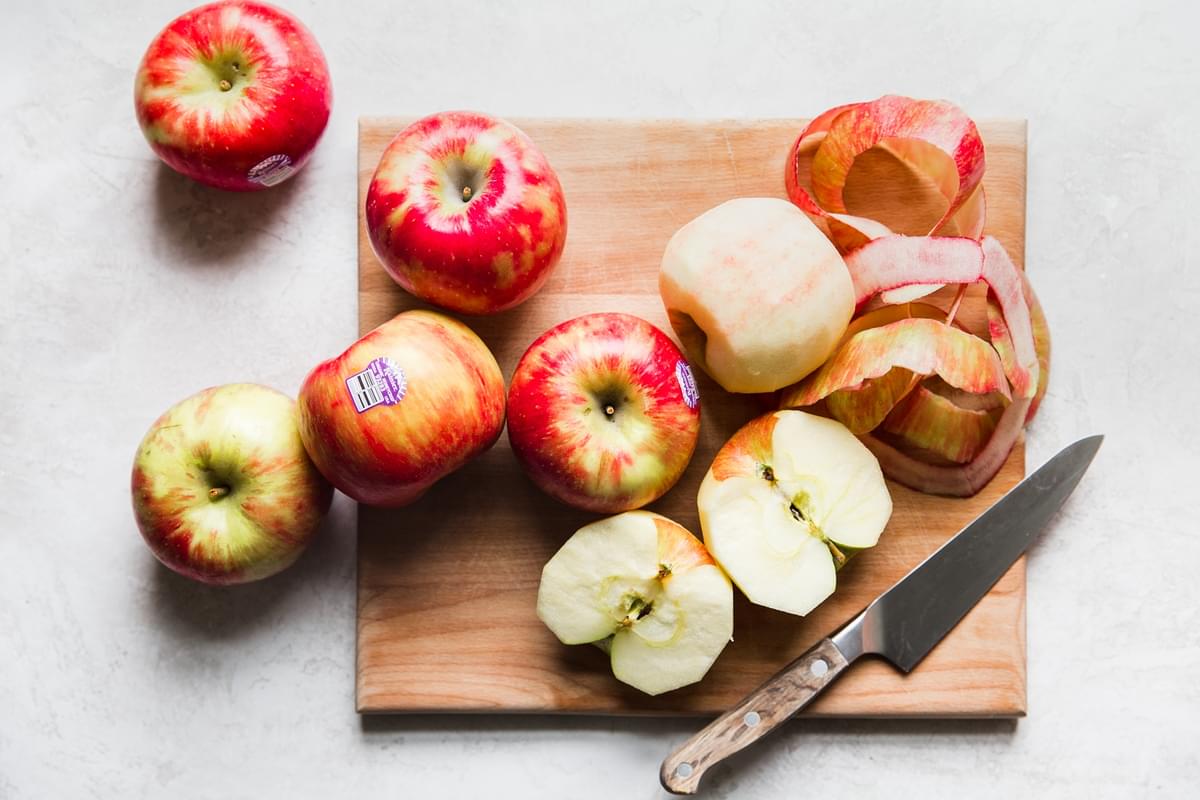 apples on a cutting board with knife, 2 of them with skin peeled off.