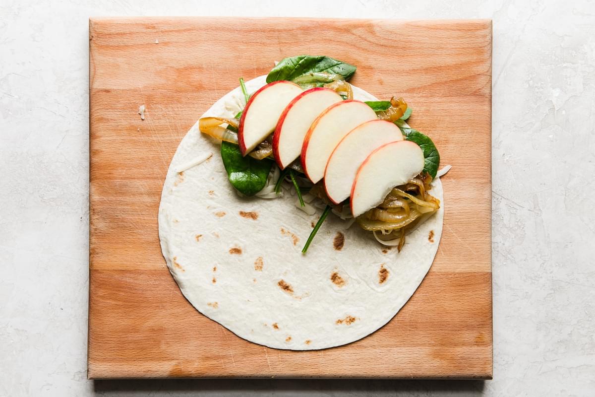 apples, caramelized onions spinach and fontina on a tortilla on a cutting board