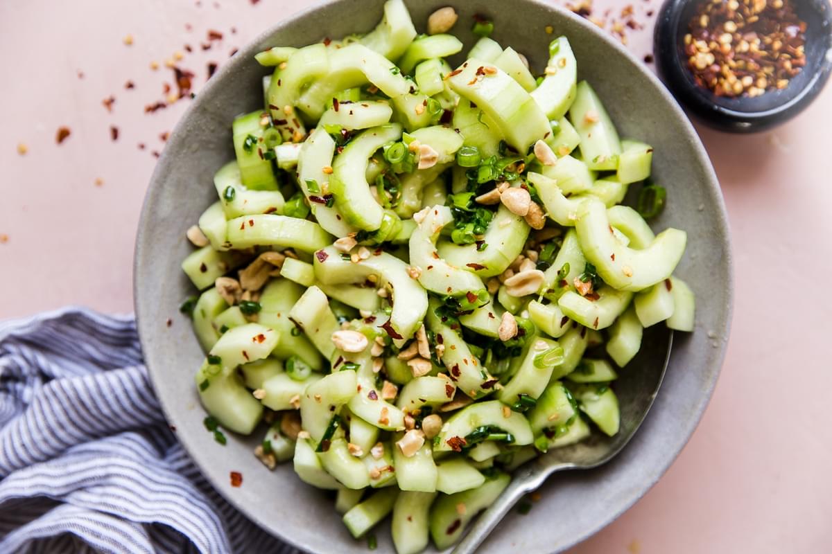 asian cucumber salad in a large bowl with a spoon with a side of red pepper flakes in a small bowl