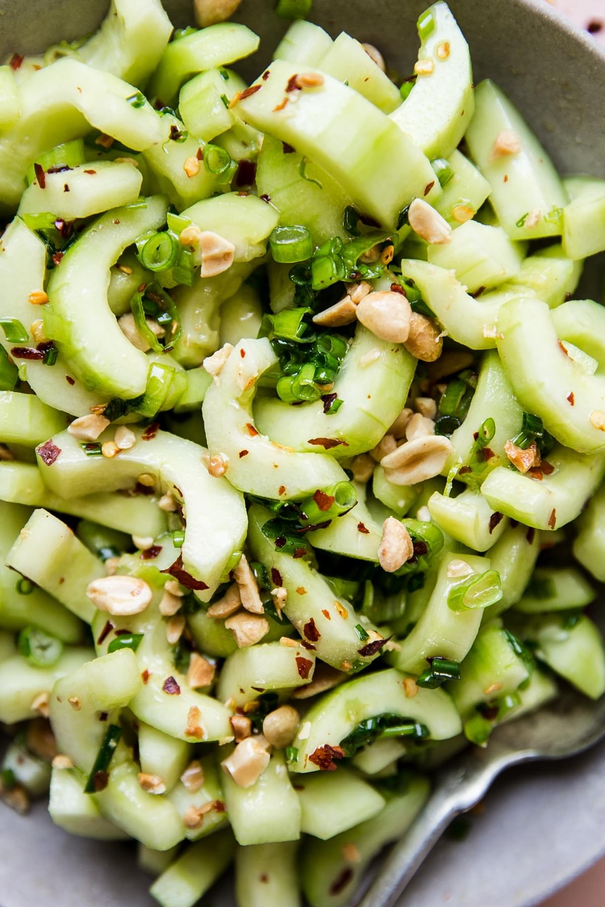 asian cucumber salad topped with crushed peanuts in a large bowl with a spoon