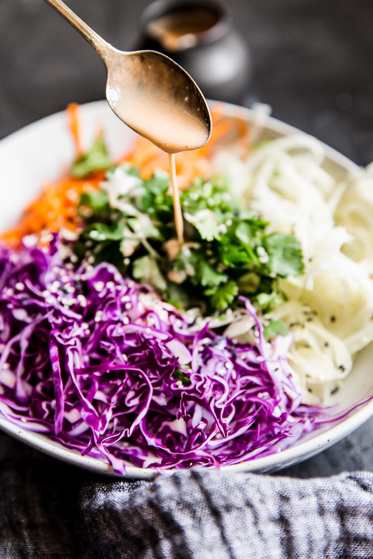 Asian Slaw With Sriracha Dressing being poured with a spoon.