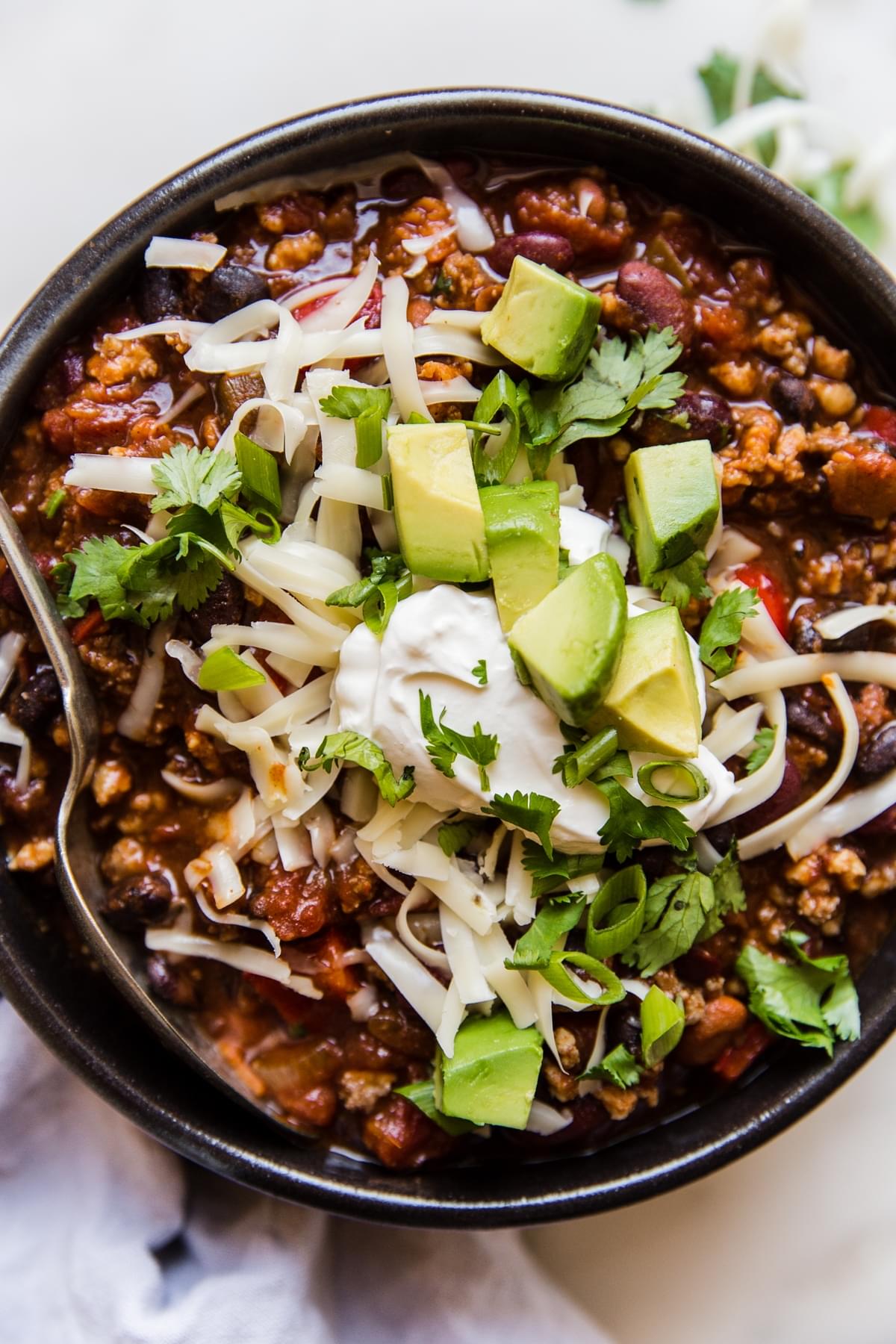 black bowl filled with award winning chili and topped with grated cheese, cilantro and diced avocados
