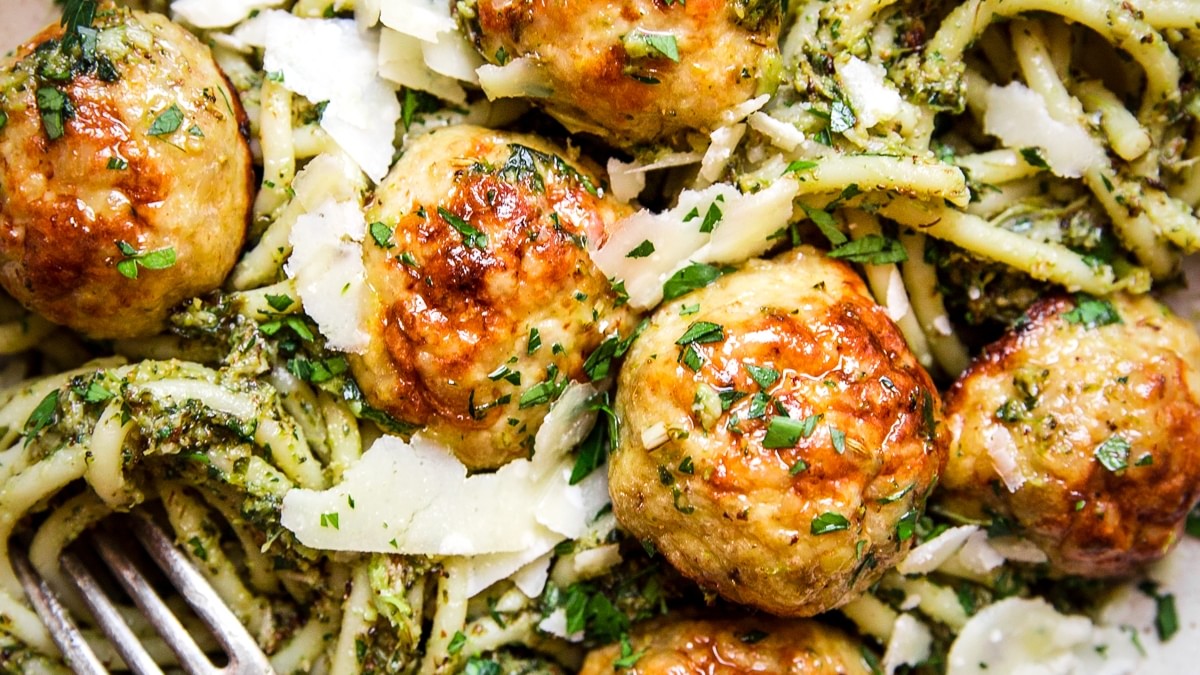 glass bowl of baked chicken meatballs with broccoli pesto pasta topped with parmesan cheese