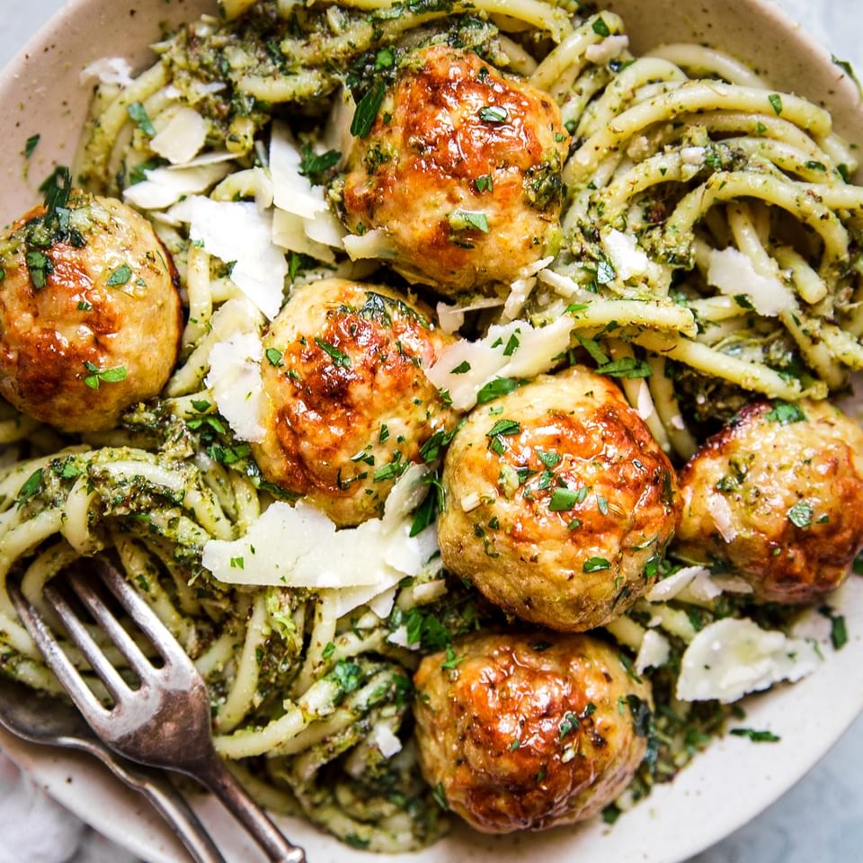 glass bowl of baked chicken meatballs with broccoli pesto pasta topped with parmesan cheese