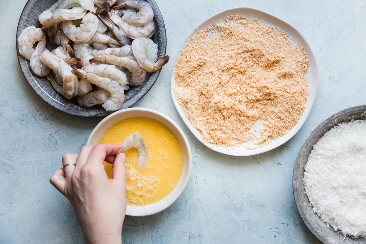 hand dipping raw jumbo shrimp in a bowl of beaten eggs