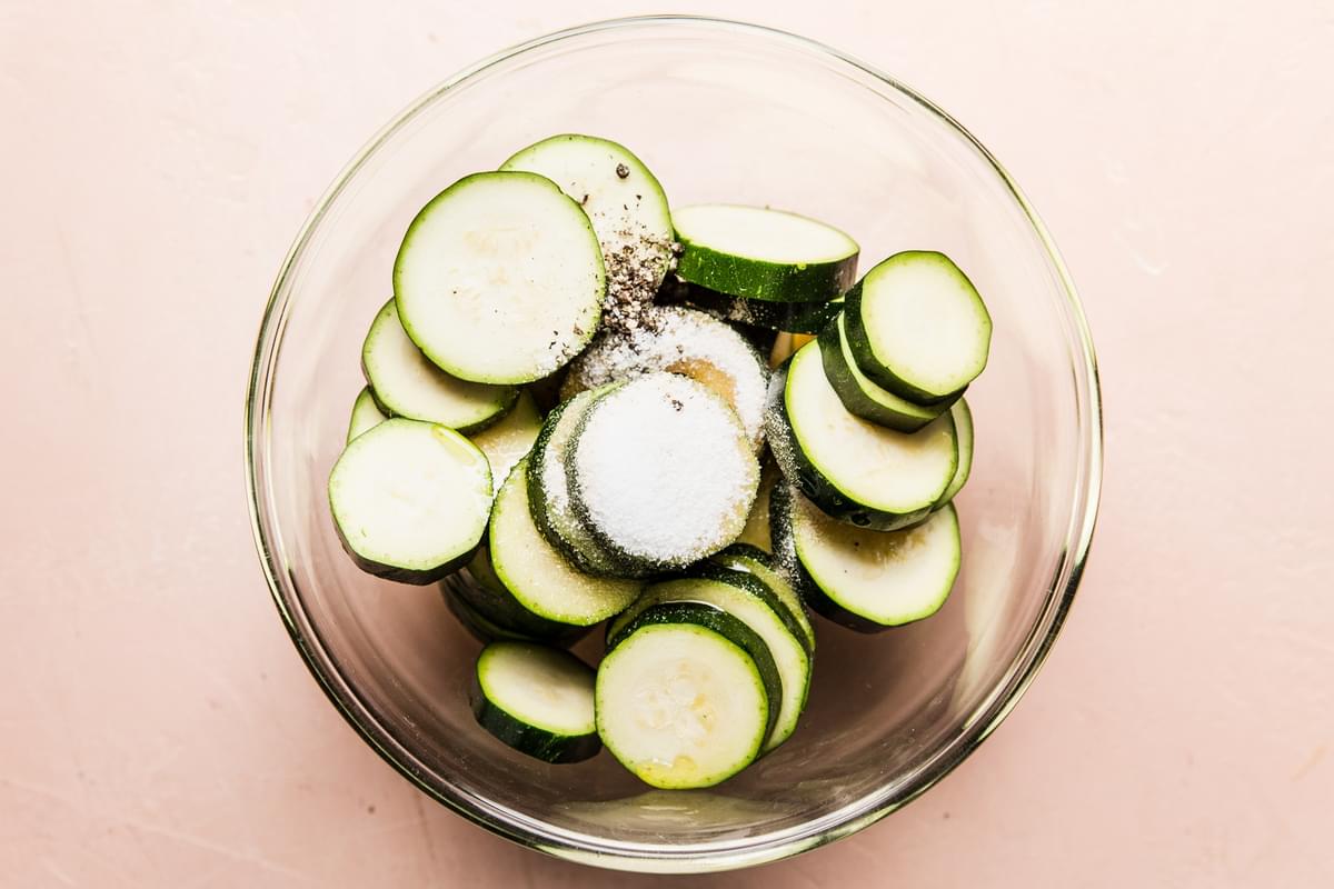 glass bowl of sliced zucchini with salt, pepper and garlic