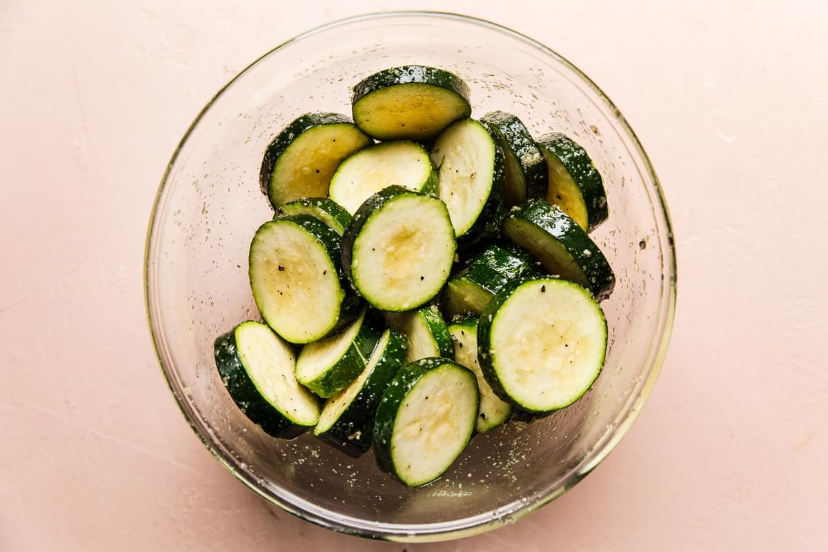 glass bowl of sliced zucchini tossed with olive oil, salt, pepper and garlic