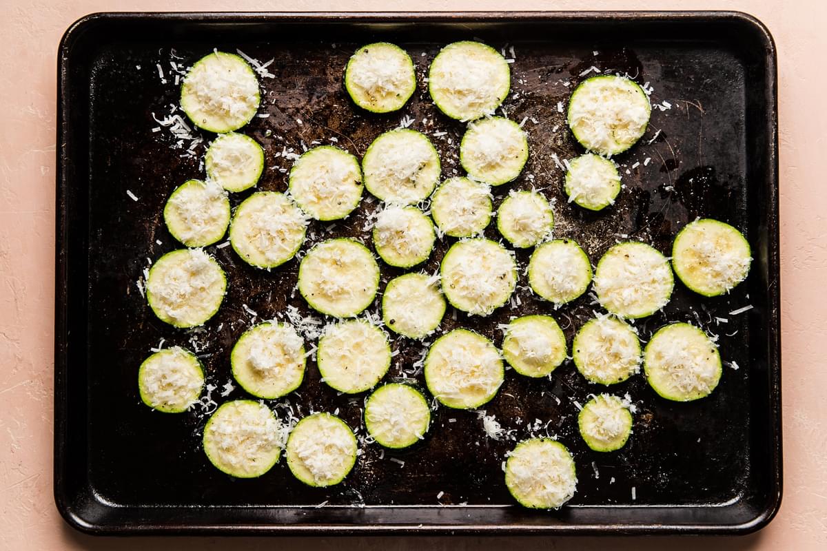 baking sheet of sliced raw seasoned zucchini topped with grated parmesan cheese