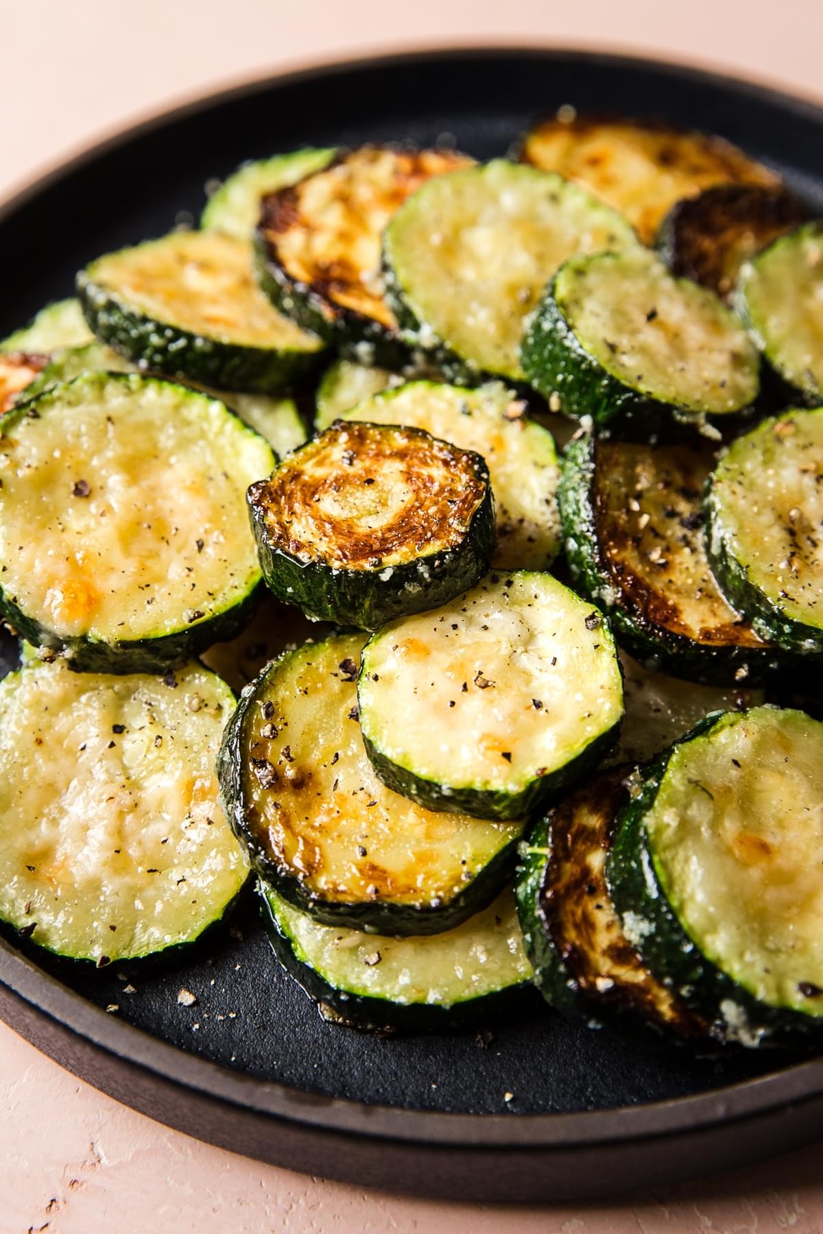 black plate of baked zucchini slices with parmesan cheese