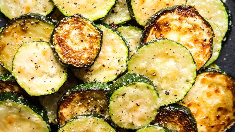 a pile of roasted zucchini with parmesan cheese on a black please