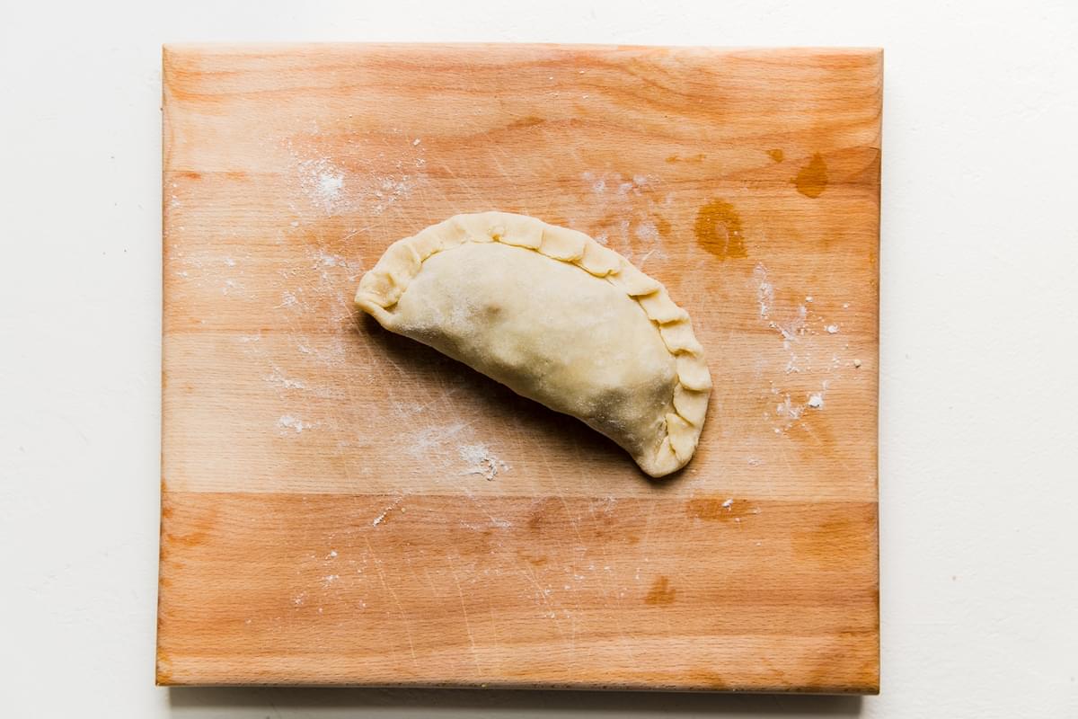 uncooked empanada on a cutting board with edges crimped together