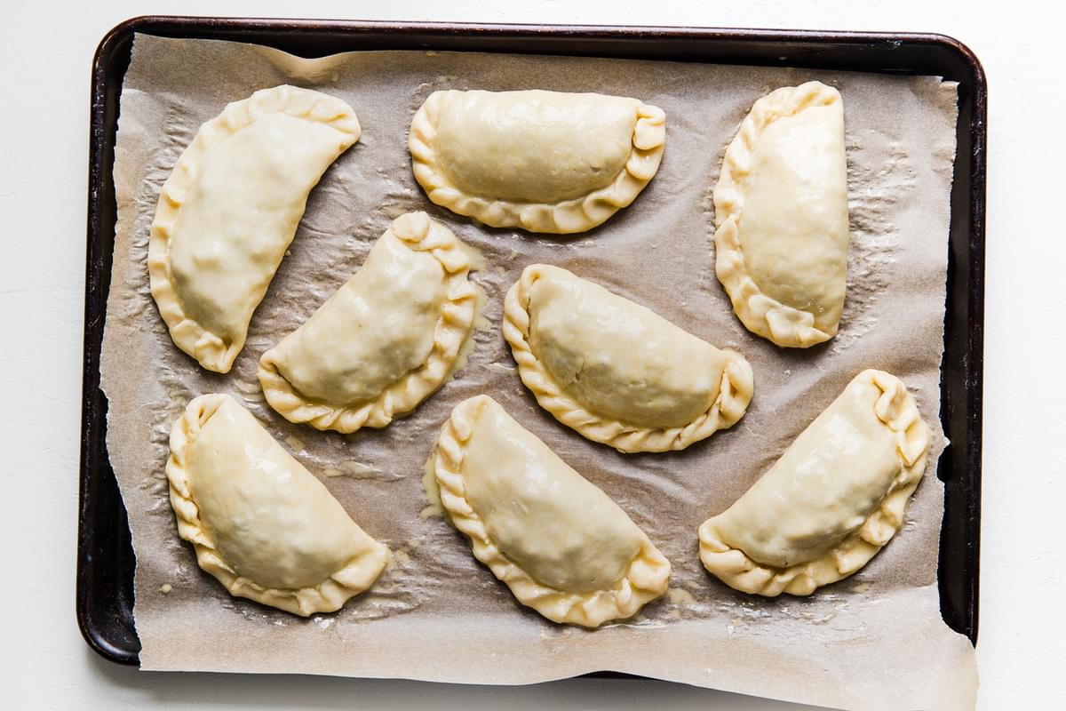uncooked empanadas on a parchment lined baking sheet