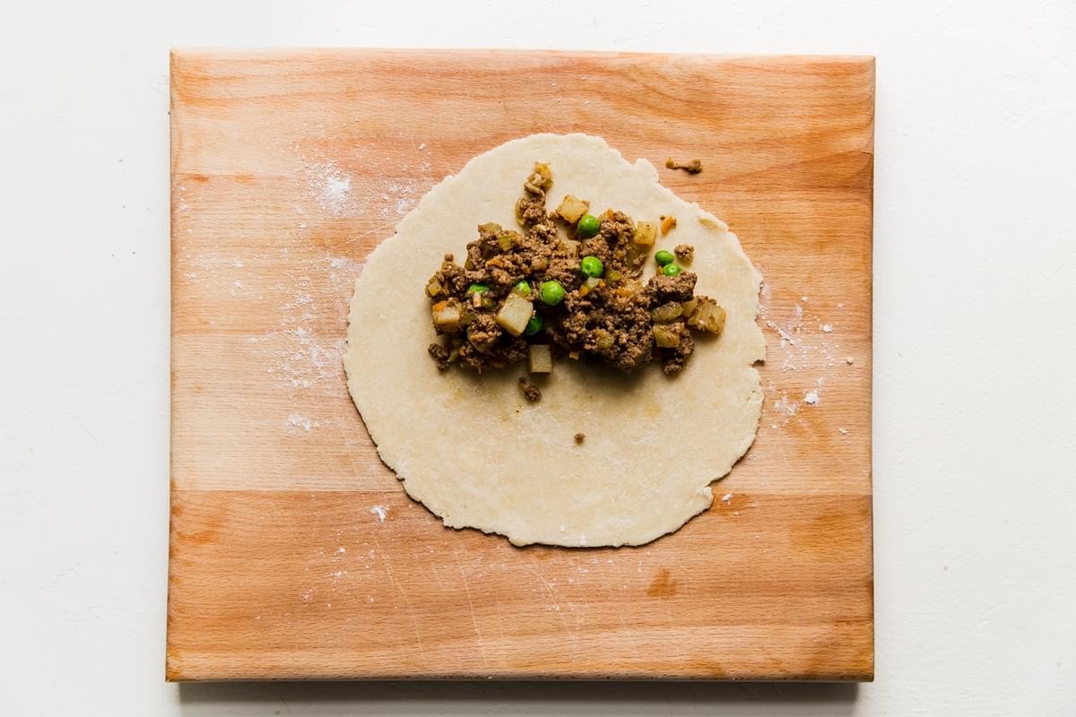empanada dough rolled out on a cutting board with beef empanada filling on one half