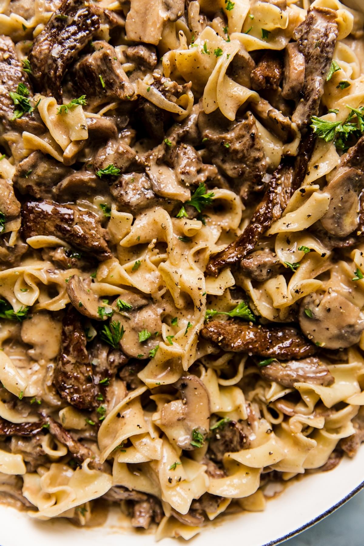 homemade beef stroganoff tossed with egg noodles and sprinkled with fresh parsley in a skillet