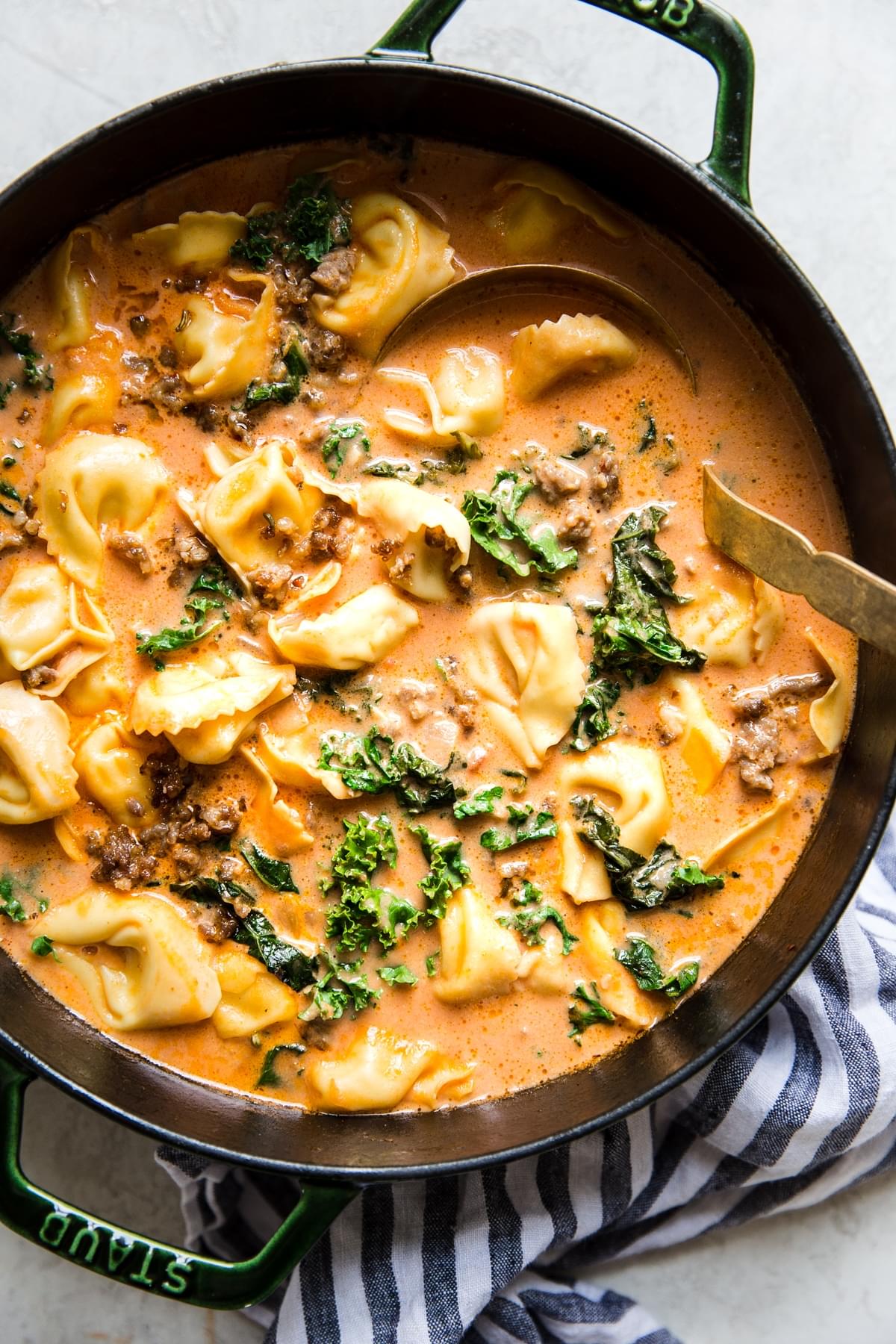 Creamy Tomato Tortellini Soup With Sausage And Kale in a pot with a ladle.