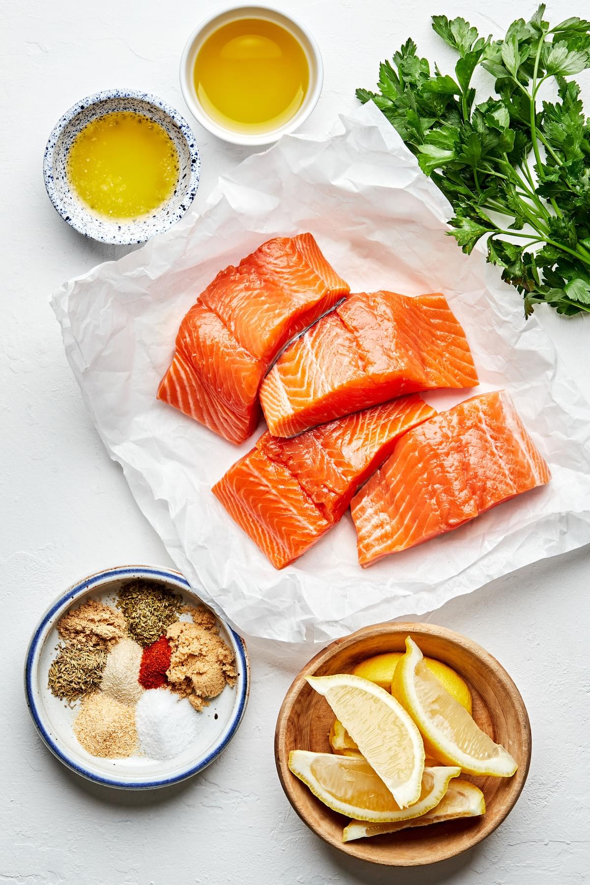 four 4-ounce raw salmon filets, melted butter, spices, lemon wedges and parsley in bowls to make blackened salmon
