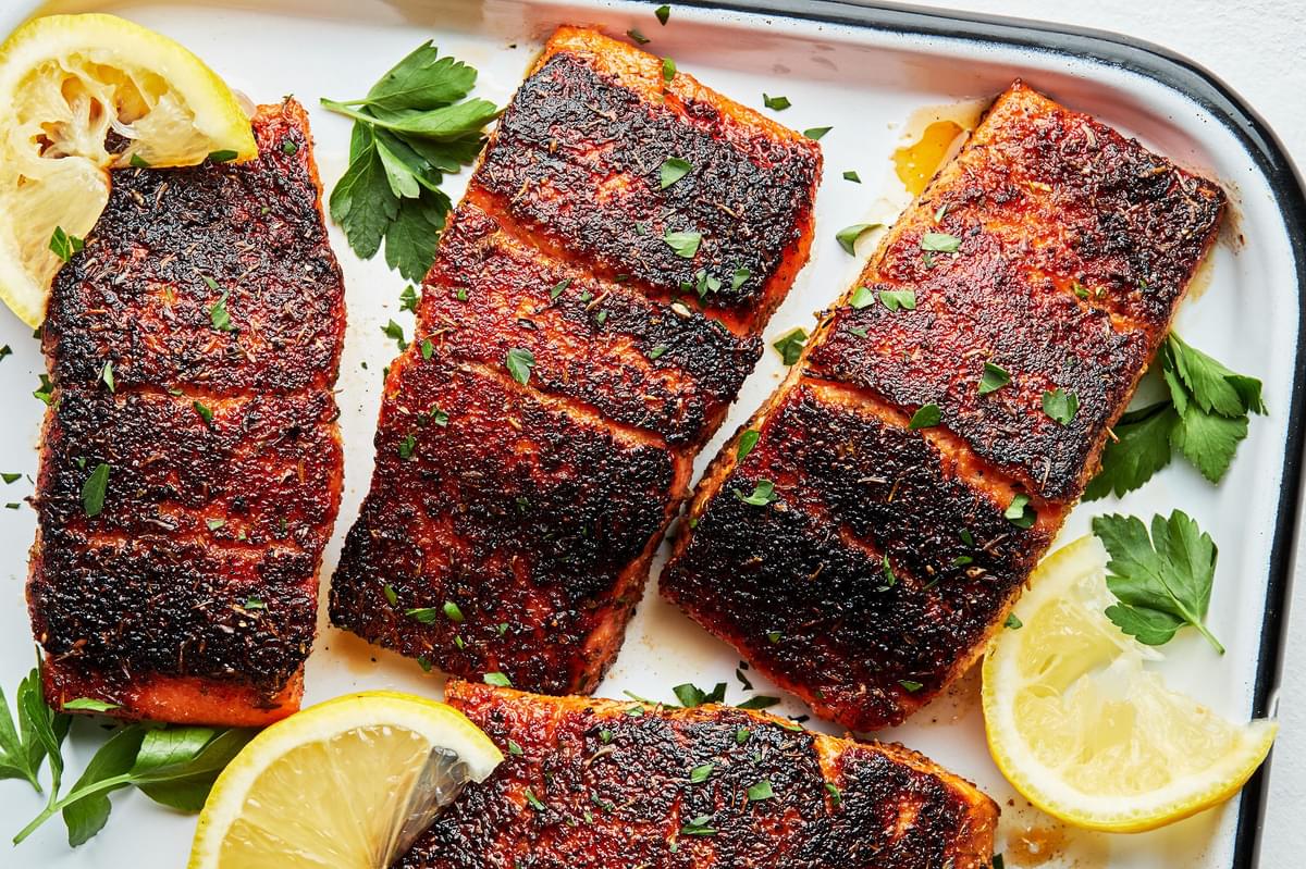 homemade blackened salmon on a serving platter with lemon wedges and sprinkled with fresh parsley