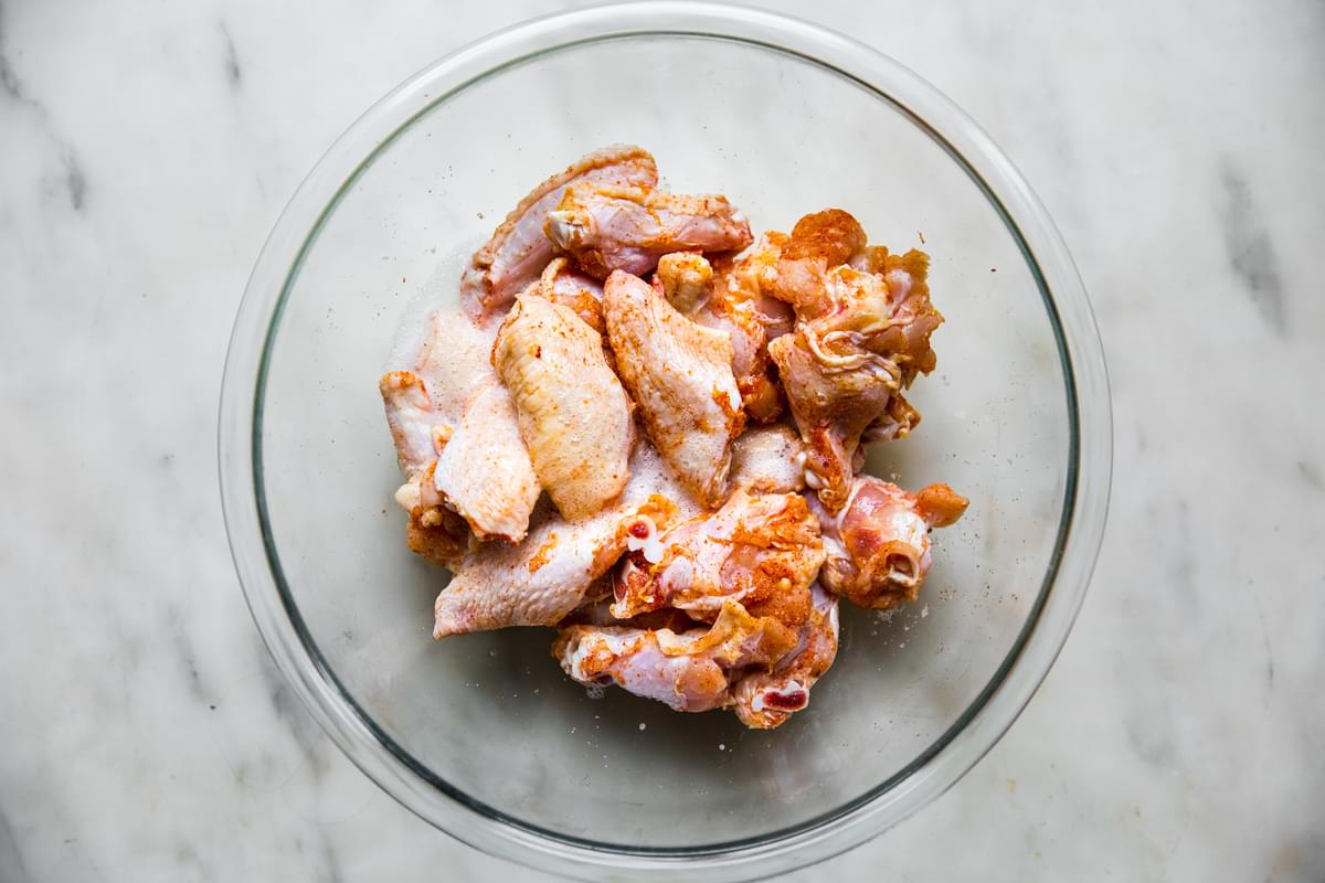 seasoned raw chicken wings tossed in egg whites in a glass bowl on the counter for baked buffalo wings