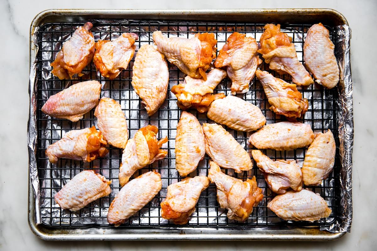 chicken wings coated with seasoning and egg whites on a cooling rack on top of a rimmed baking sheet lined with foil