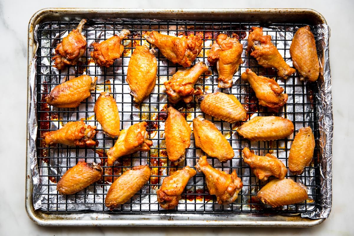 baked chicken wings on a cooling rack on top of a rimmed baking sheet lined with foil sitting on the counter
