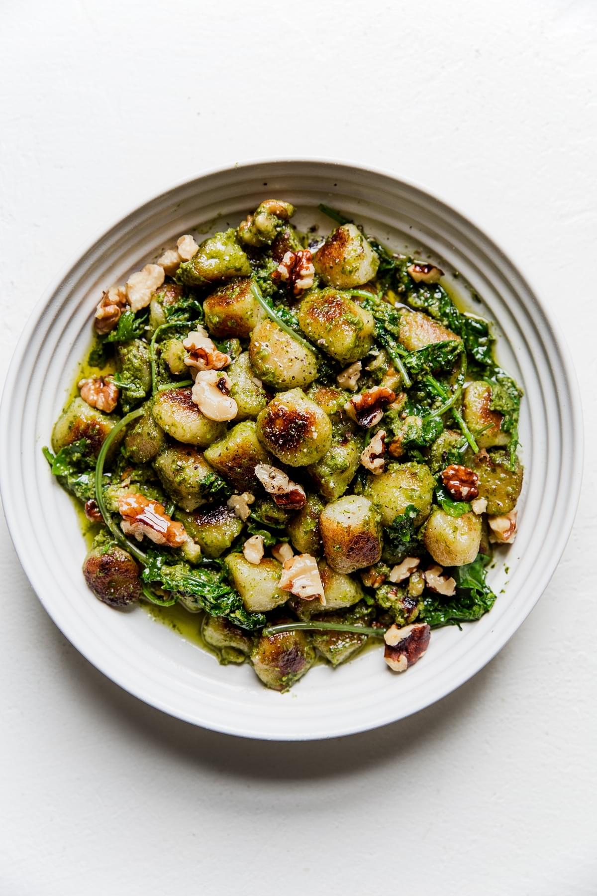 vegan Cauliflower gnocchi with kale-cashew pesto topped with toasted walnuts in a white bowl