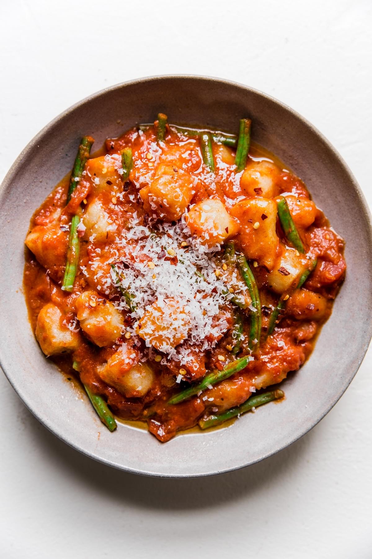 vodka sauce and green bean cauliflower gnocchi topped with fresh parmesan cheese in a bowl