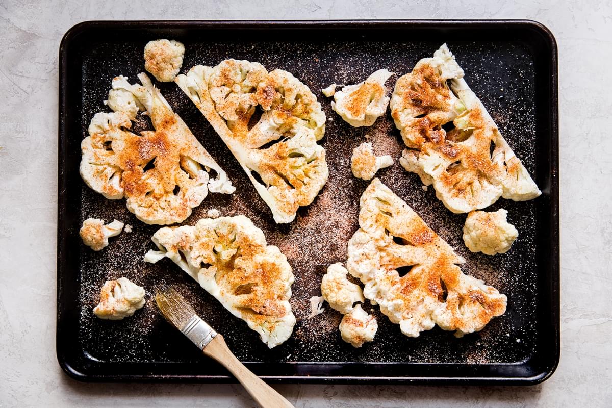 cauliflower steaks sliced on a baking sheet topped with olive oil and spices