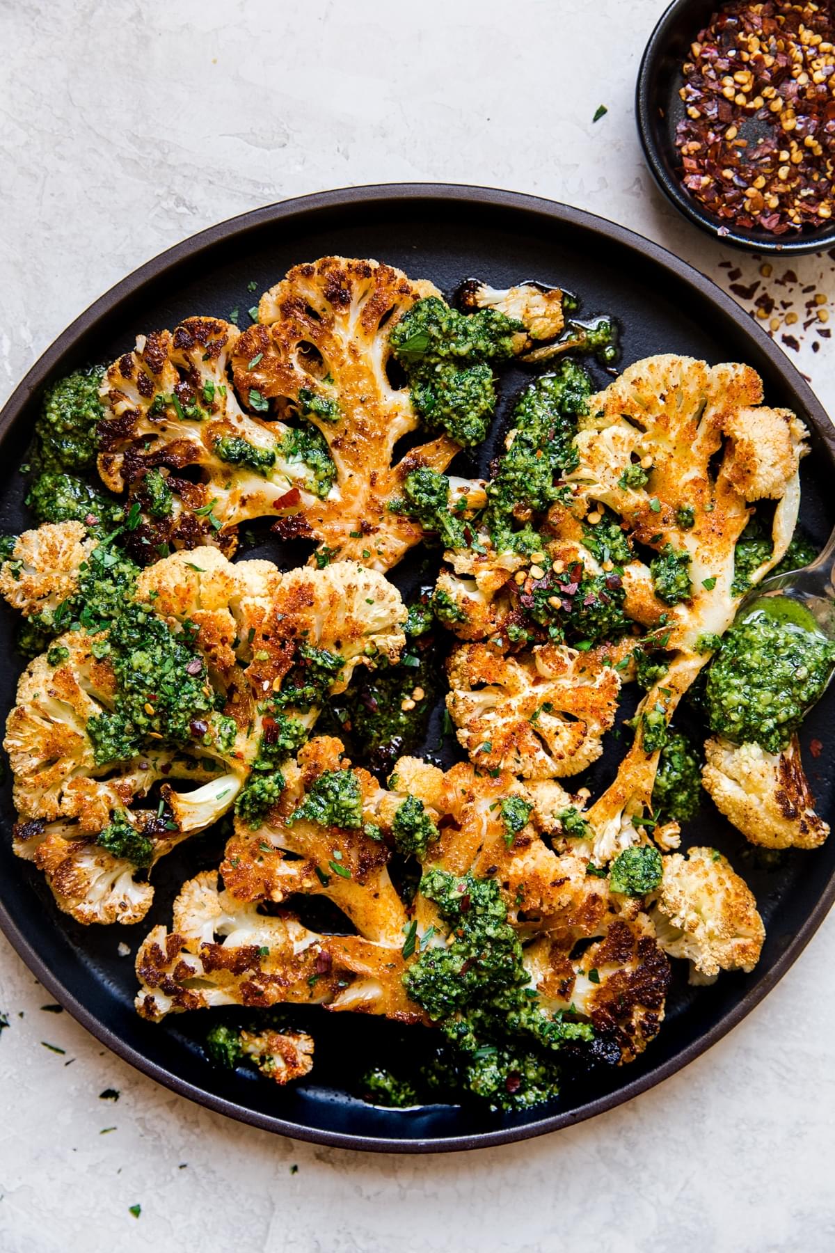 black plate of cauliflower topped with walnut kale pesto and red pepper flakes