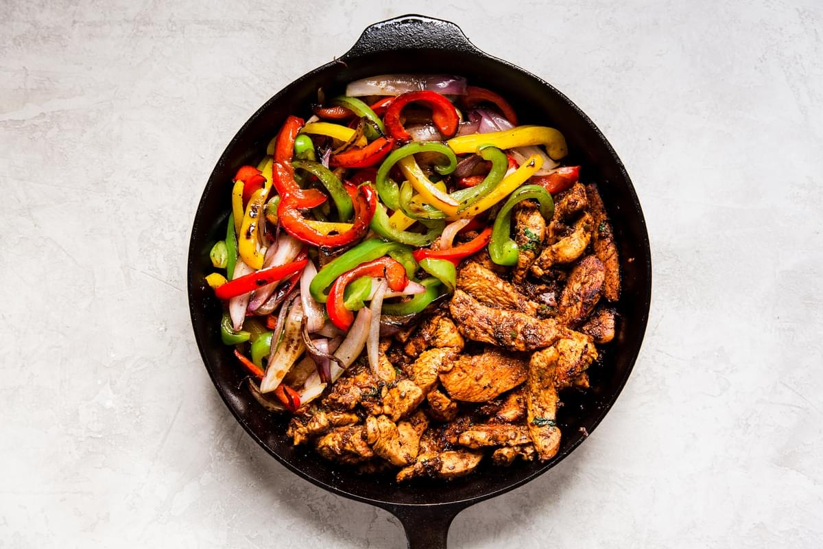 cast iron skillet of cooked fajita chicken, red, green and yellow bell peppers and onions