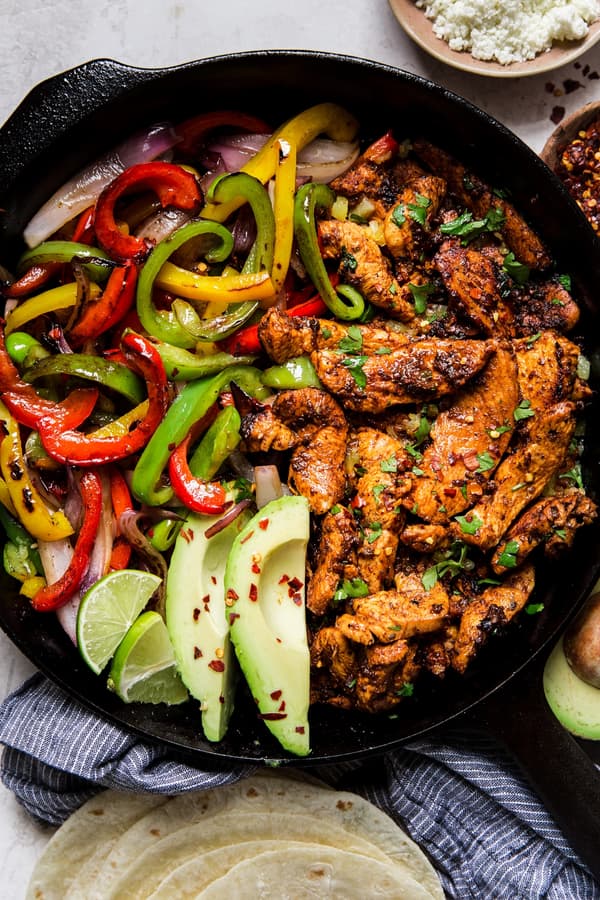 chicken fajitas in a cast iron skillet with bell peppers, avocado, and fresh limes