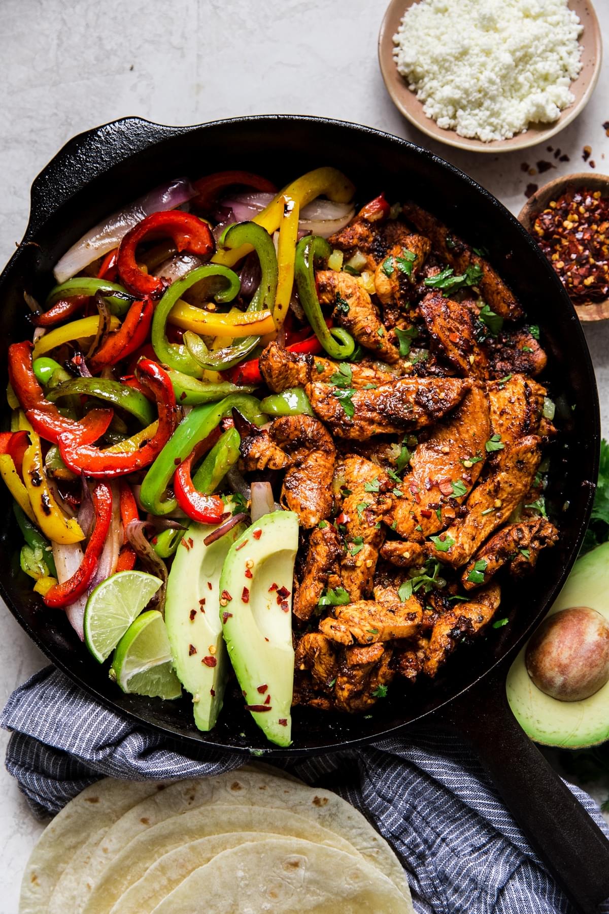 cast iron skillet of chicken fajitas with tortillas on the side