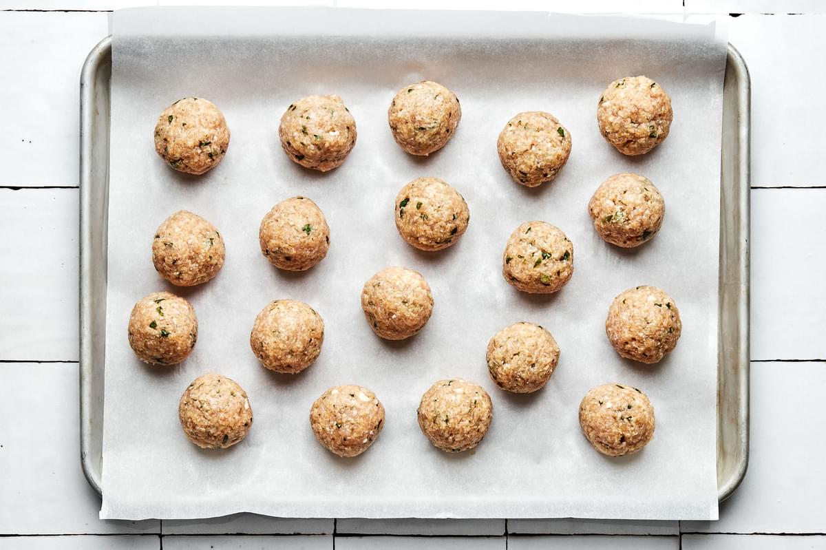 raw homemade chicken meatballs on a parchment lined baking sheet